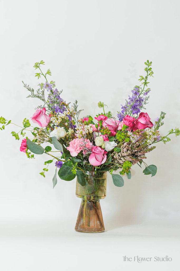 This serene and elegant arrangement features four soft lavender roses, symbolizing love and calm, surrounded by the regal purple larkspur that evokes deep emotion.