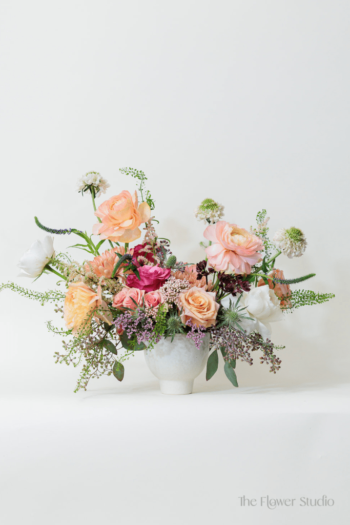 Elegance meets vibrant charm in this breathtaking floral arrangement, showcasing a delicate blend of soft peaches, purples, and whites.
