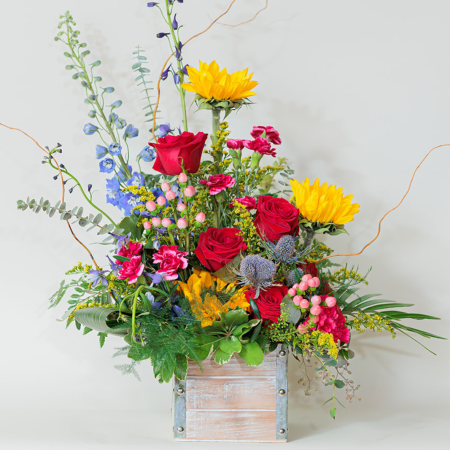 This bold and eye-catching flower arrangement in a rustic wooden box is a beautiful fusion of vibrant hues and rich textures, creating a dynamic and contemporary design.