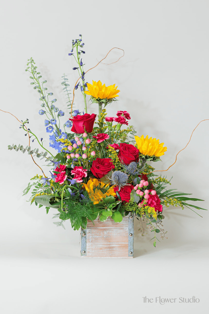This bold and eye-catching flower arrangement in a rustic wooden box is a beautiful fusion of vibrant hues and rich textures, creating a dynamic and contemporary design.