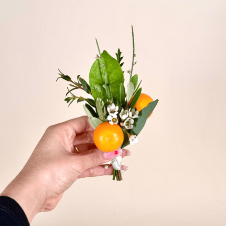 A charming boutonniere inspired by a sunlit citrus grove, this piece combines the elegance of white filler with a vibrant pop of color.
