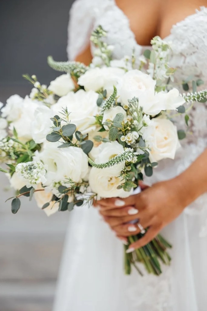 A close-up of a bride holding a beautiful bouquet of white roses and lush greenery, showcasing elegance and sophistication.
