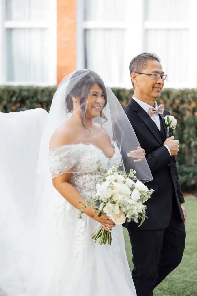 Bride walking down the aisle with her father, both smiling, in a beautiful outdoor setting.