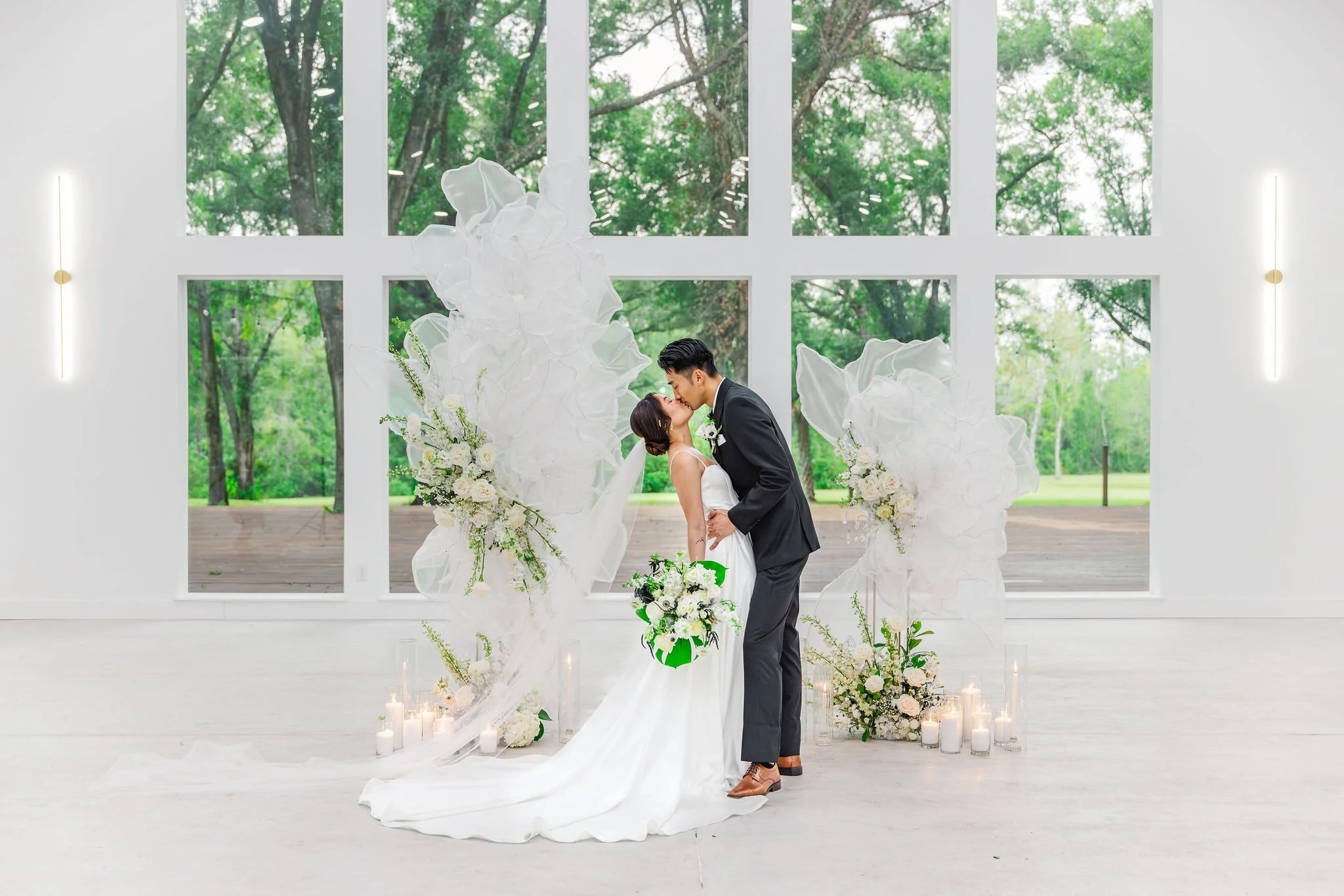 A bride and groom sharing a kiss in an elegantly decorated venue, surrounded by floral arrangements and candles.