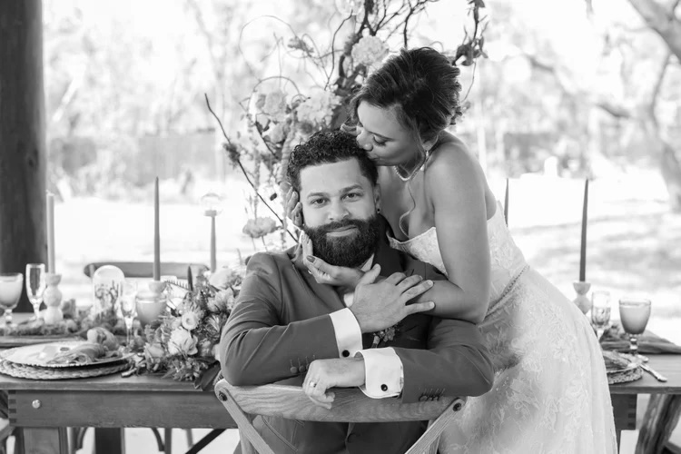 A couple sharing an intimate moment at a beautifully styled table setting, surrounded by floral arrangements and soft candlelight, exuding a sense of romance and elegance.