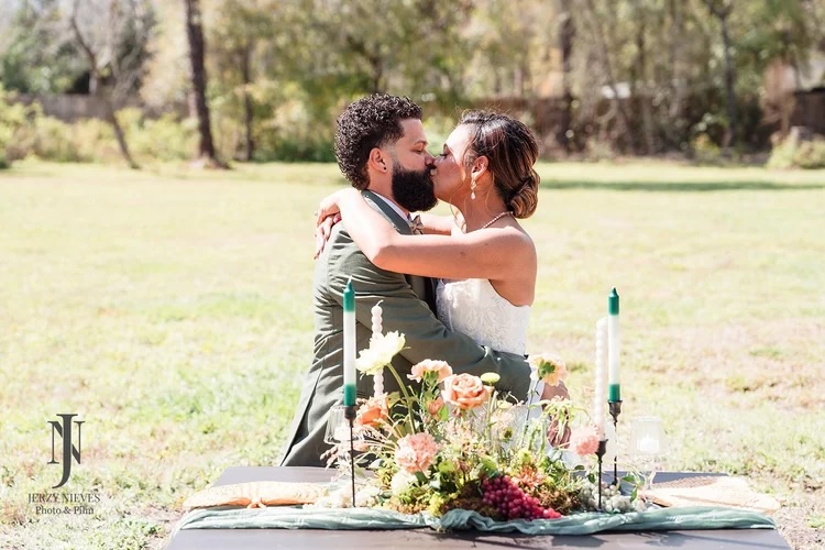 A couple embracing in a romantic outdoor setting, surrounded by a beautifully styled table with flowers and candles.